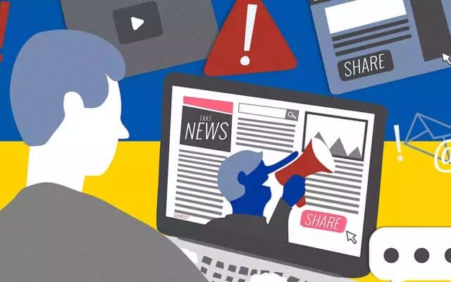 A person in front of a Ukraine flag looking at misinformation on a computer.